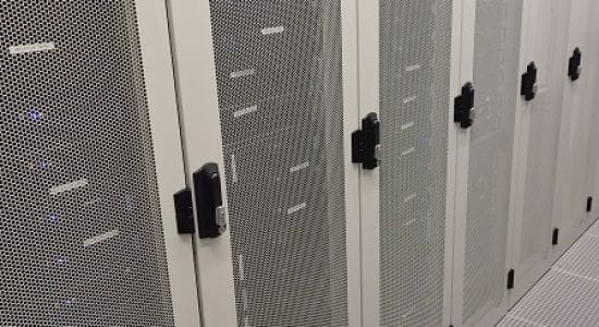 Couloir central dans un datacenter, flanqué de baies de serveurs fermées et en fonctionnement, avec un sol conçu pour un refroidissement optimal, symbolisant une infrastructure serveur avancée et sécurisée.