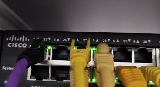 Switch Cisco actif et connecté dans une baie de serveur, avec de multiples câbles réseau branchés et fonctionnels, symbolisant une connectivité réseau fiable et performante.