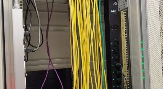 Vue arrière d'une baie de serveur avec deux commutateurs Cisco et un système de redémarrage à distance PDU APC. Câblage organisé descendant vers le bas avec des lumières indiquant que le système est en fonctionnement.